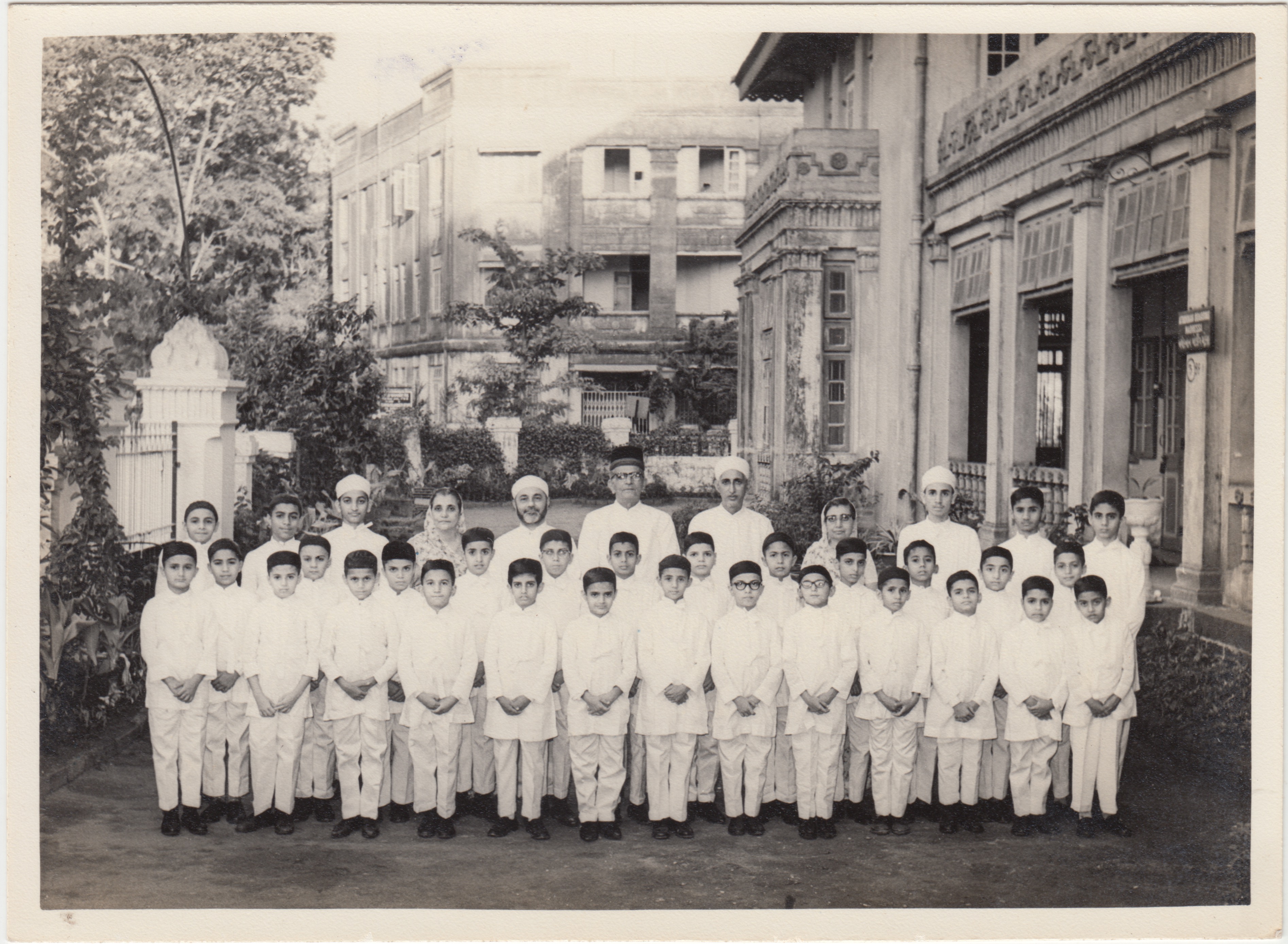 Black-and-white photograph of students in white duglis with staff and teachers outside the Madressa